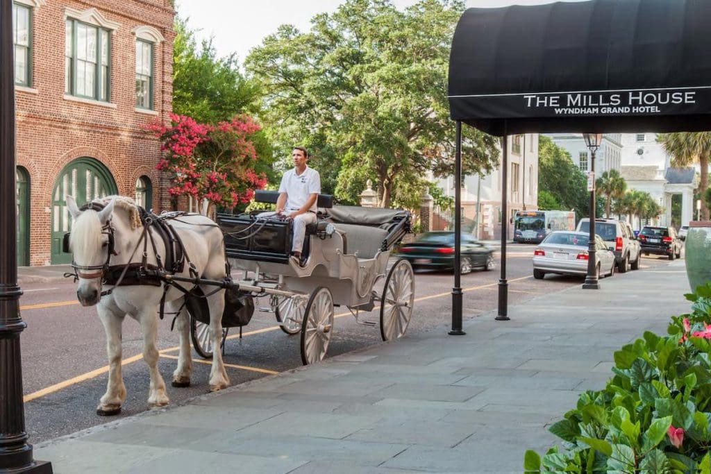 A horse-drawn carriage sits outside the entrance to the The Mills House Wyndham Grand Hotel on a sunny day.