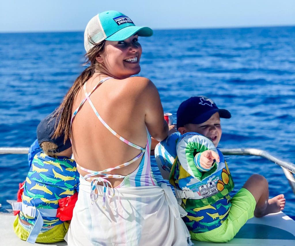 A woman sitting on a boat turns around laughing, while her two kids sit in front of her, and the ocean beyond.