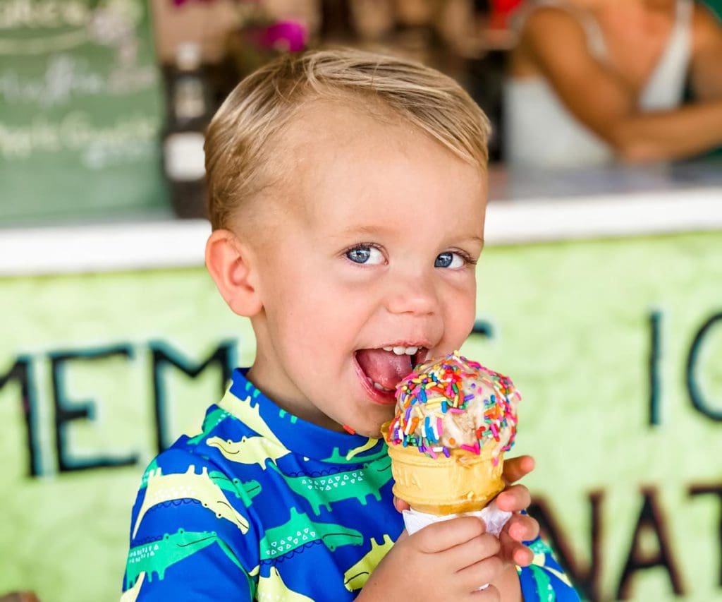 A young boy smiles broadly as he eats an ice cream cone with sprinkles.