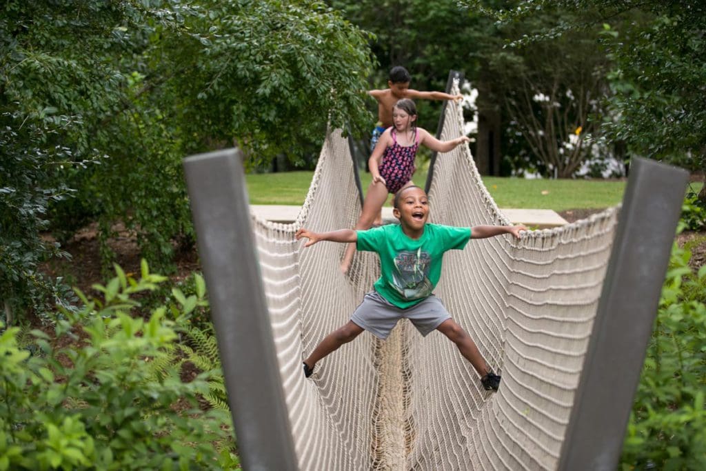 Three kids work their way across a large rope-style bridge at the Atlanta Botanical Garden, one of the best places to stop on an NYC to Miami itinerary for families!