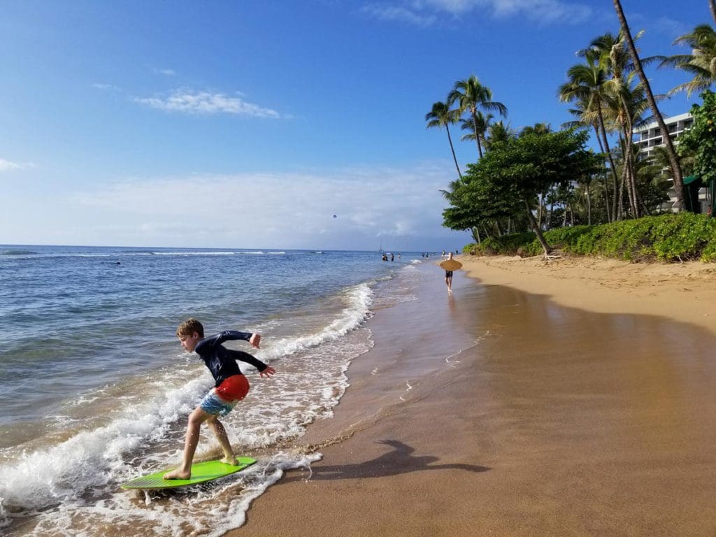 A young boy boogie boards along an oceanfront in Hawaii.