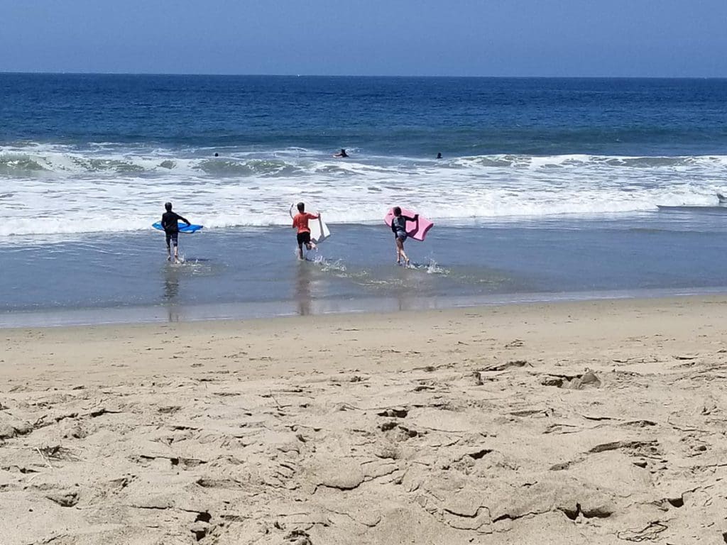 Three kids race to the ocean with boogie boards in their hands, one of the best things to do in Los Angeles with teens.