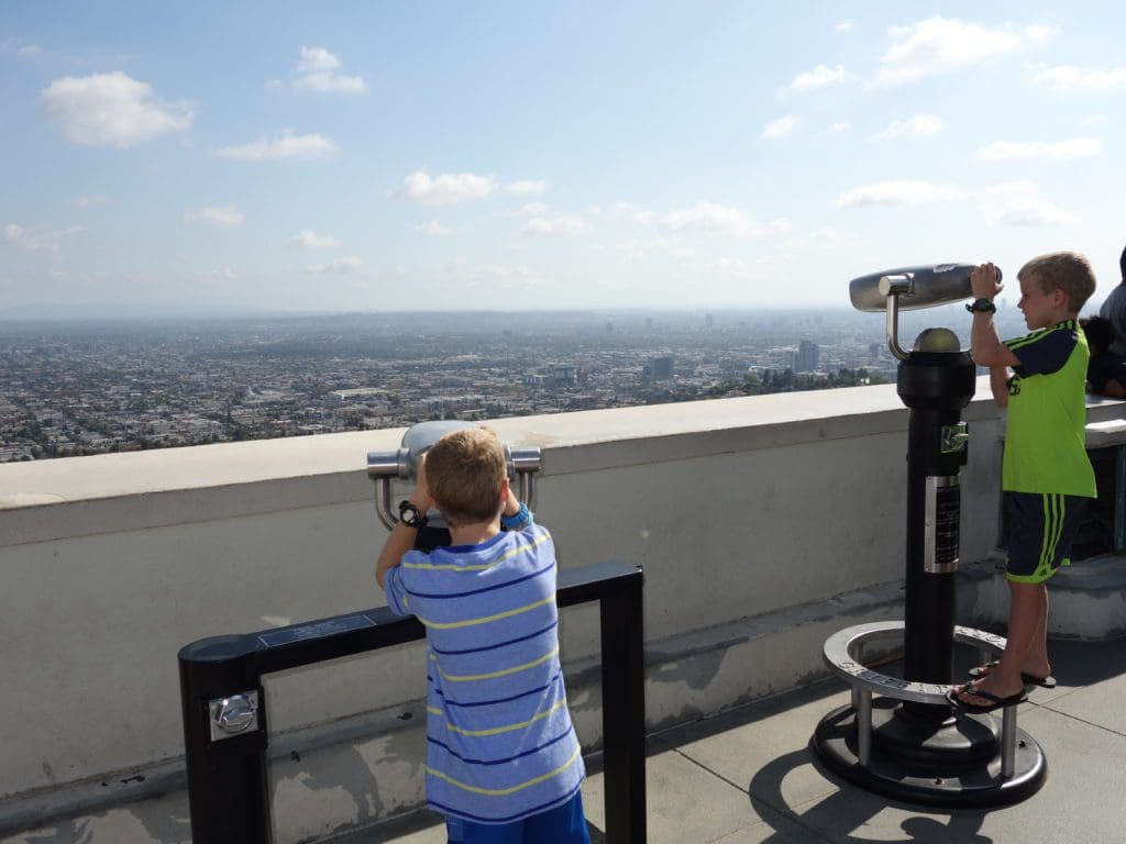 Two tween boys look through observation viewers on top of the Griffith Observatory in LA, one of the best things to do in Los Angeles with teens this summer.