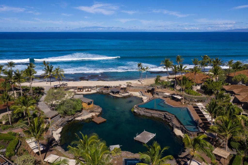 The large pool, surrounded by palms, and near the ocean shore at Four Seasons Resort Hualalai.