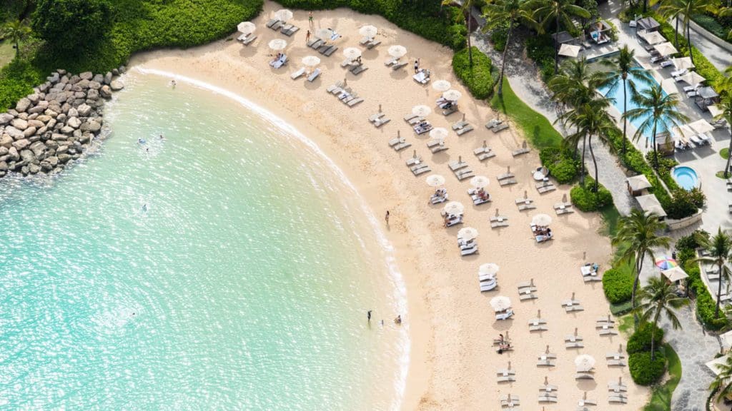 An aerial view of the pristine beach and lined beach cabanas at Four Seasons Resort O'ahu Ko Olina, one of the best luxury hotels in the U.S for families. 