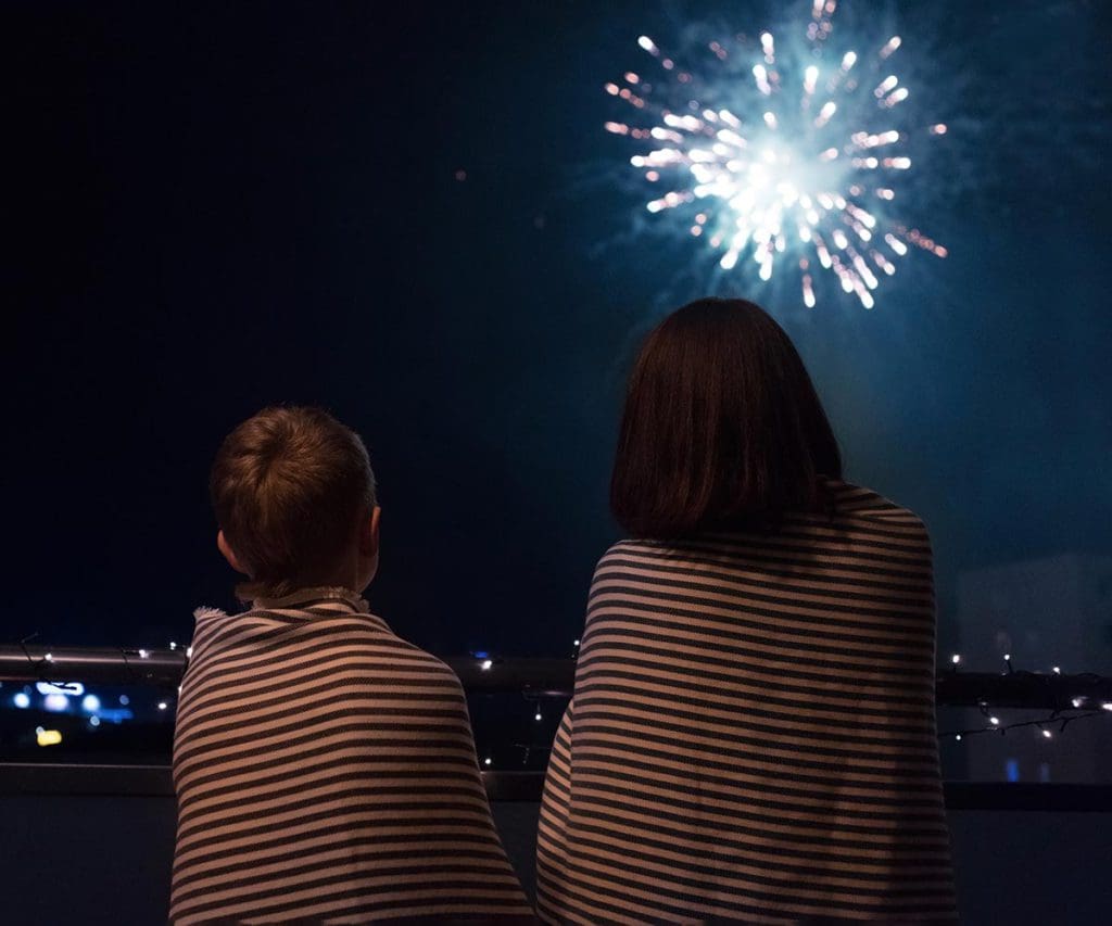 Two kids, wrapped in blankets, look up at Fourth of July fireworks.