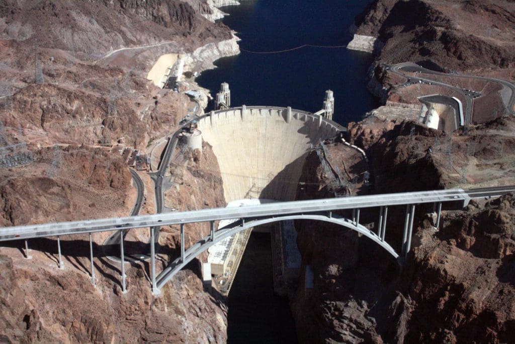 An aerial view of Hoover Dam, featuring the extensive bridge in front of the dam, dam, and water on both sides.