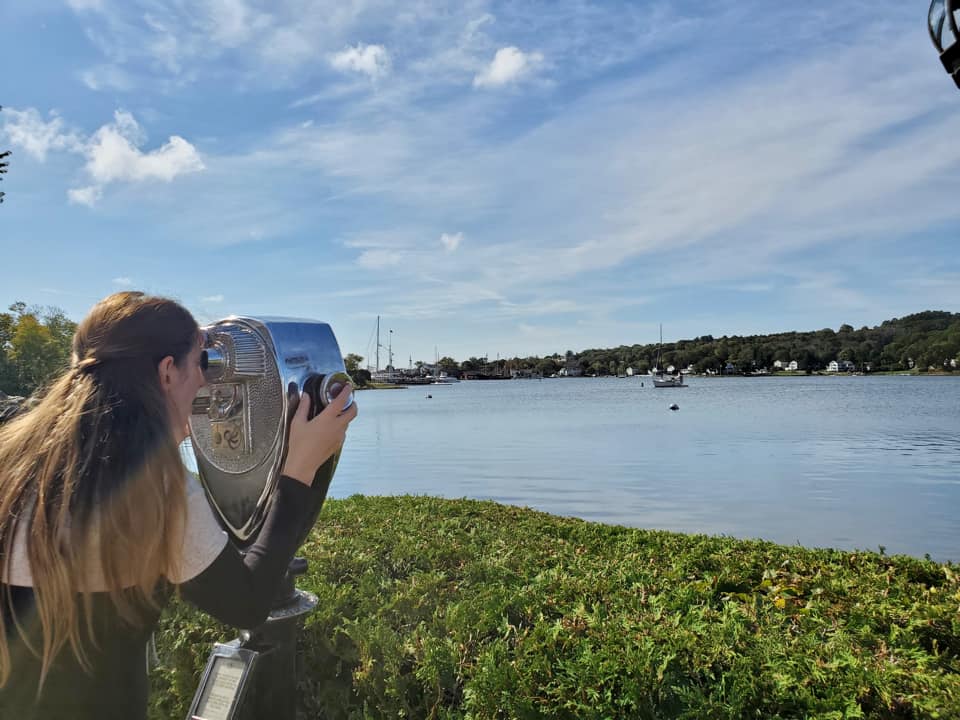 A teenage girl peers through sightseeing binoculars over the river at Mystic River Park.