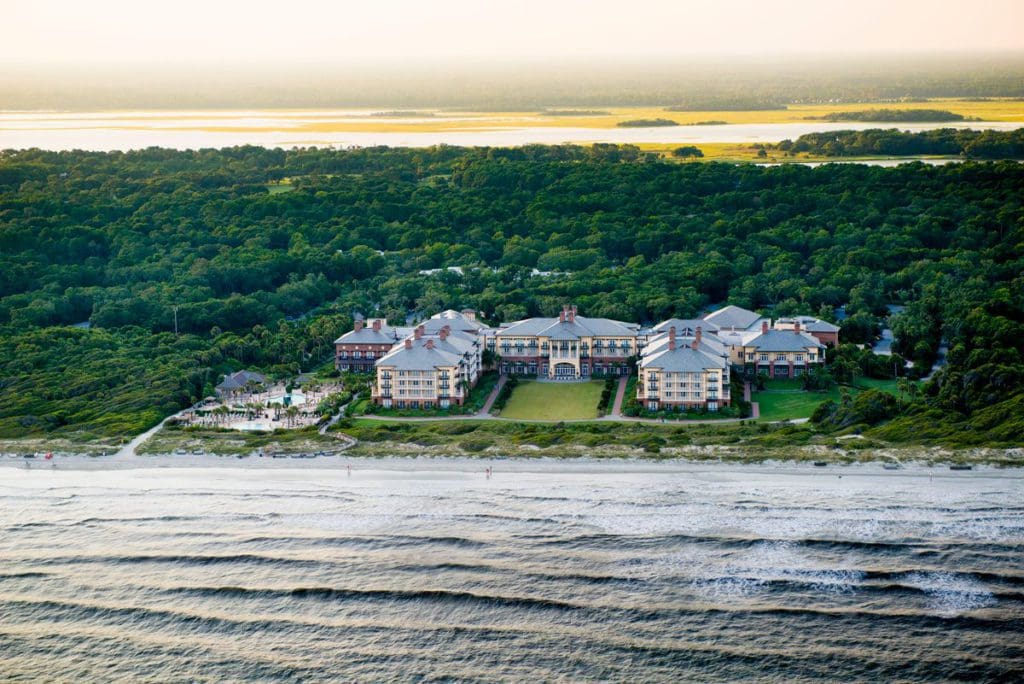 An aerial view of Kiawah Island Golf Resort, featuring lush grounds, an oceanside location, and a beautiful sunset.