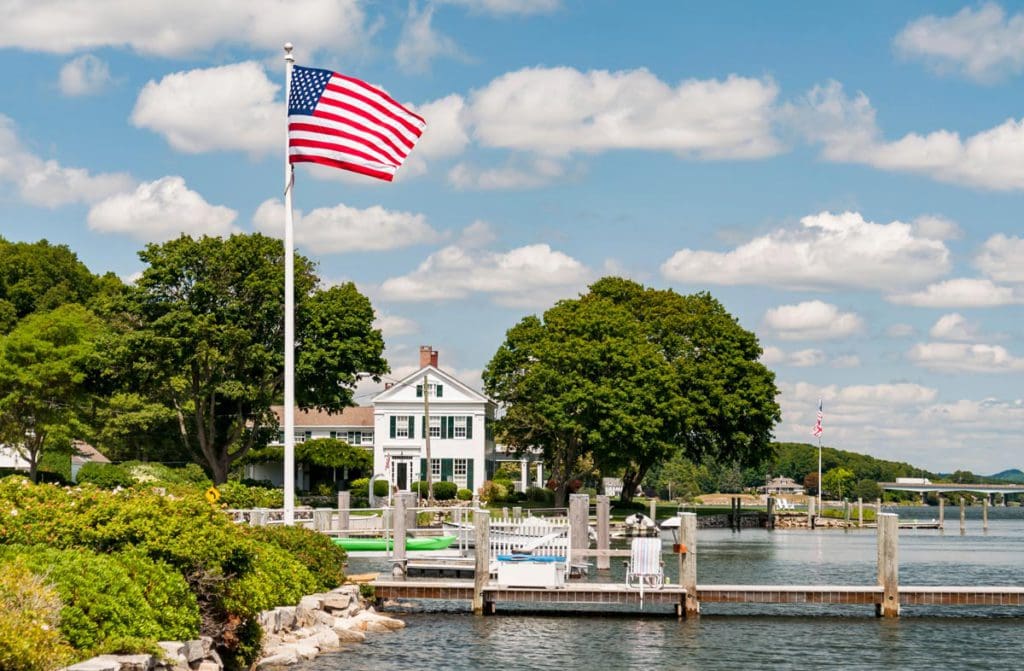 A large American flag flies overhead near the seaport at Mystic on a sunny day.