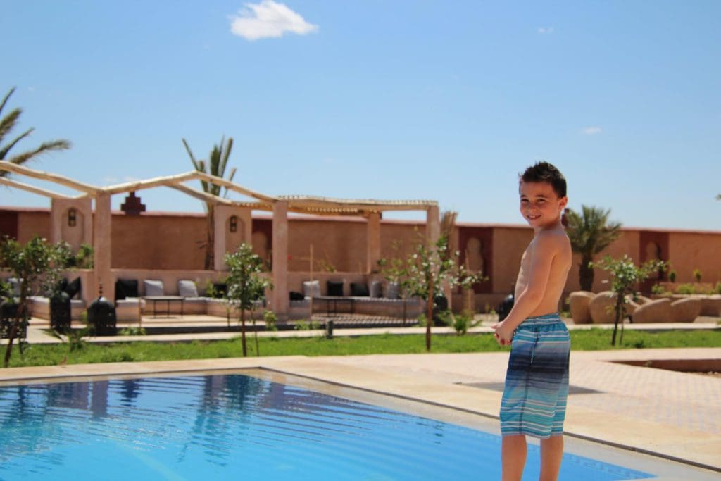 Inside a luxe accommodations, a young boy smiles near a pool, surrounded by beautiful furnishings in Morocco.