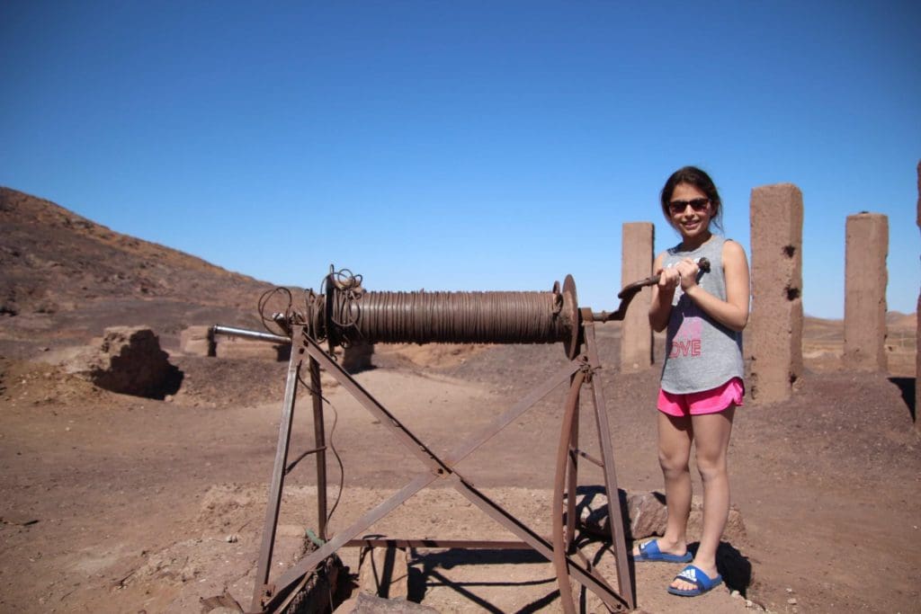 A young girl spins a large handle with a pulley system in the Moroccan desert.