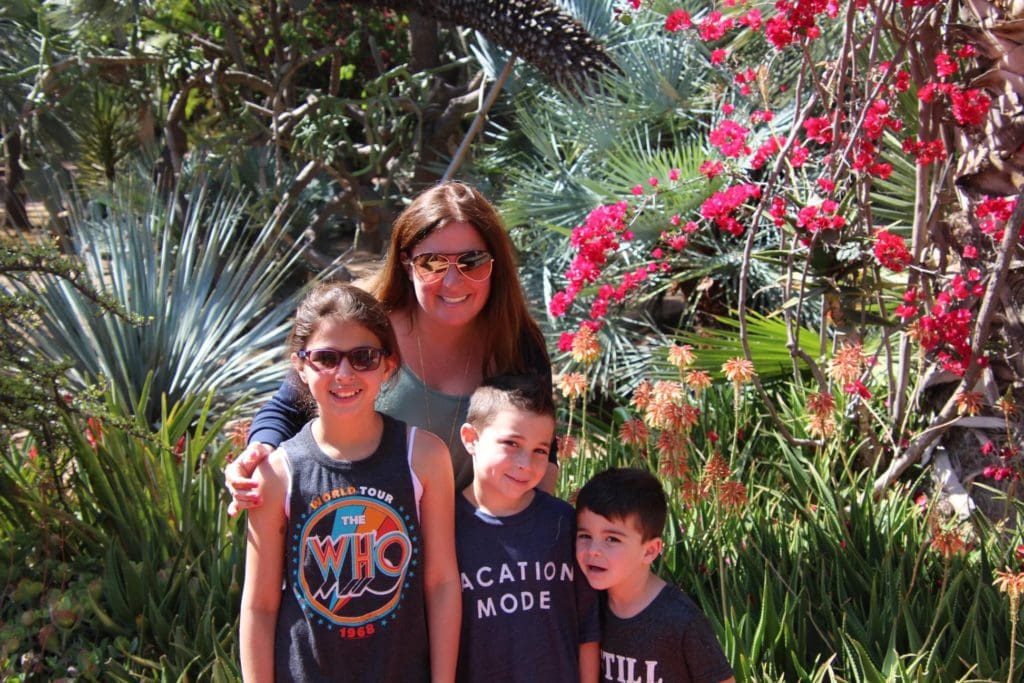 A woman and her three kids stand amongst lush greenery and flowers.