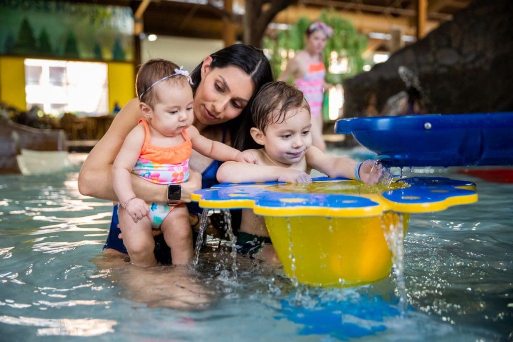 A mom holds her two young children as they play in a shallow pool area at Timber Ridge Lodge & Waterpark, one of the best Midwest hotels with indoor water parks for families.