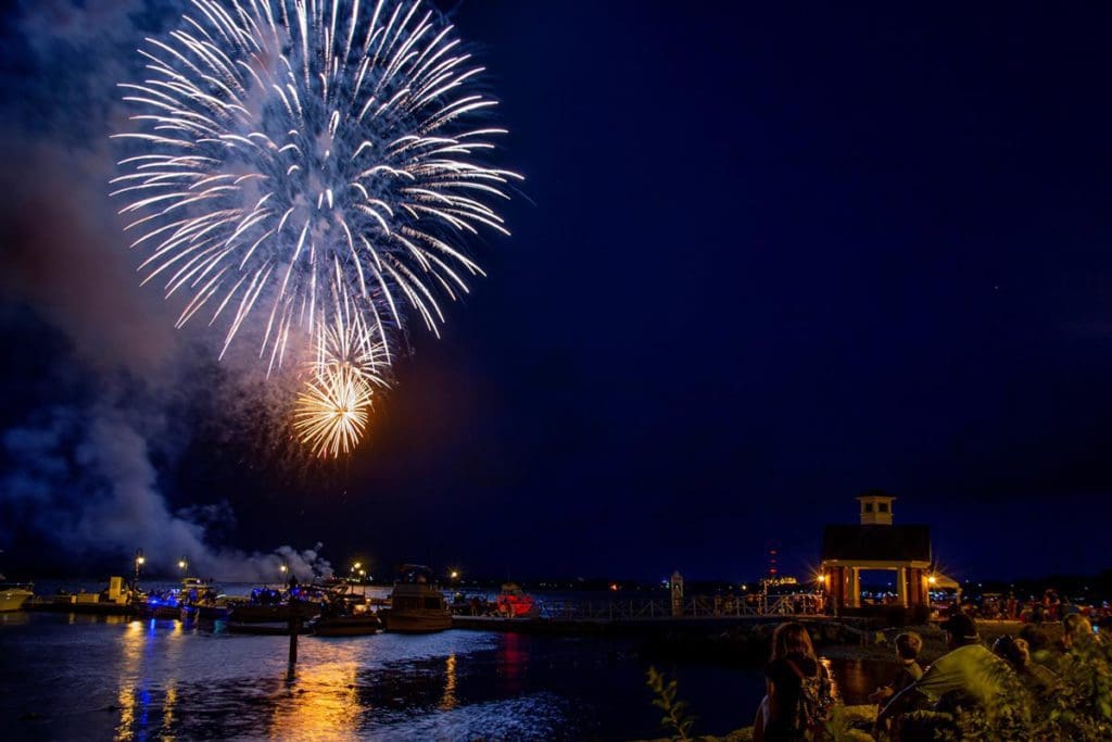 Several people watch huge fireworks from shore in Yorktown, near Williamsburg, one of the best Fourth of July destinations for a family trip.