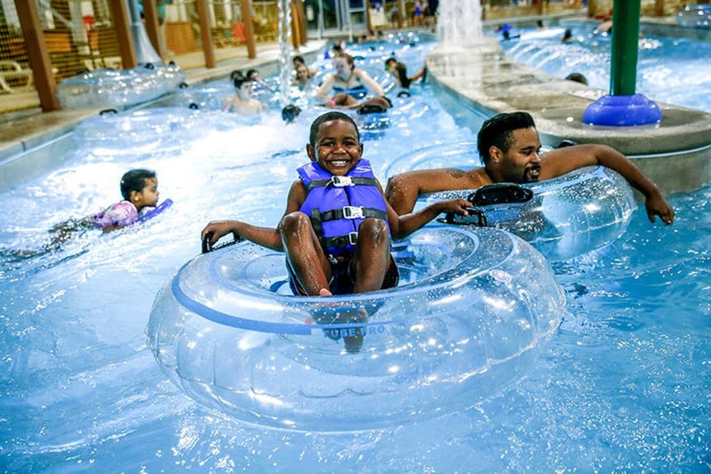 A young boy floats along the lazy river at Zehnder’s Splash Village Hotel and Water Park, while his parent walks along behind him.