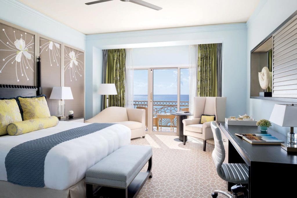 Inside one of the king bedroom guest rooms at The Ritz-Carlton, Grand Cayman, featuring cool blue colors and a large balcony.