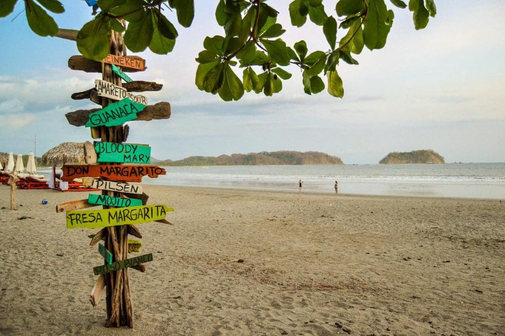Stock image of Playa Samara, showcasing a stunning beach and shoreline, with a beach sign pointing to various restaurants.