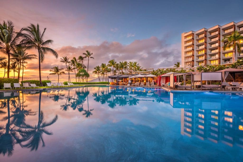 The pool at Andaz Maui at Wailea Resort - a Concept by Hyatt, with resort buildings in the background at sunset.