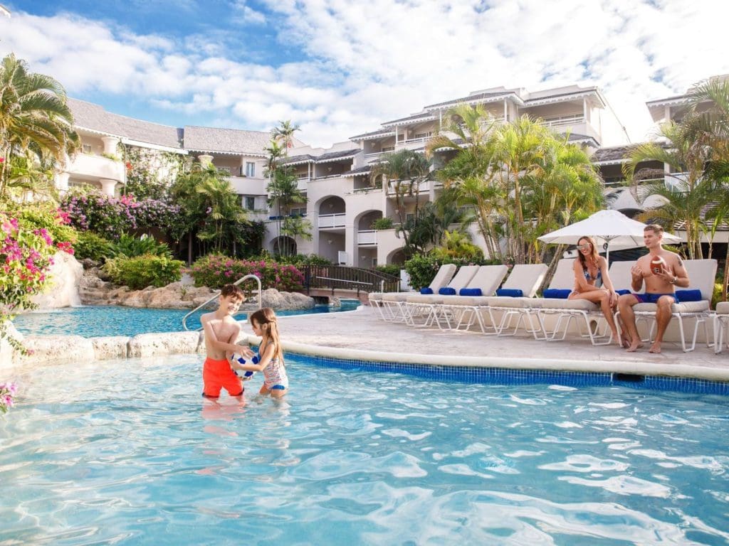 Parents sit in pool-side loungers, while watching their kids play in the pool at Bougainvillea Barbados.