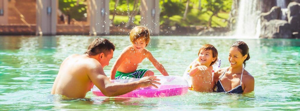 A family of four plays in the pool, with a large pink flotation device, at Hilton Waikoloa Village, one of the best Hilton Hotels in the United States for families.