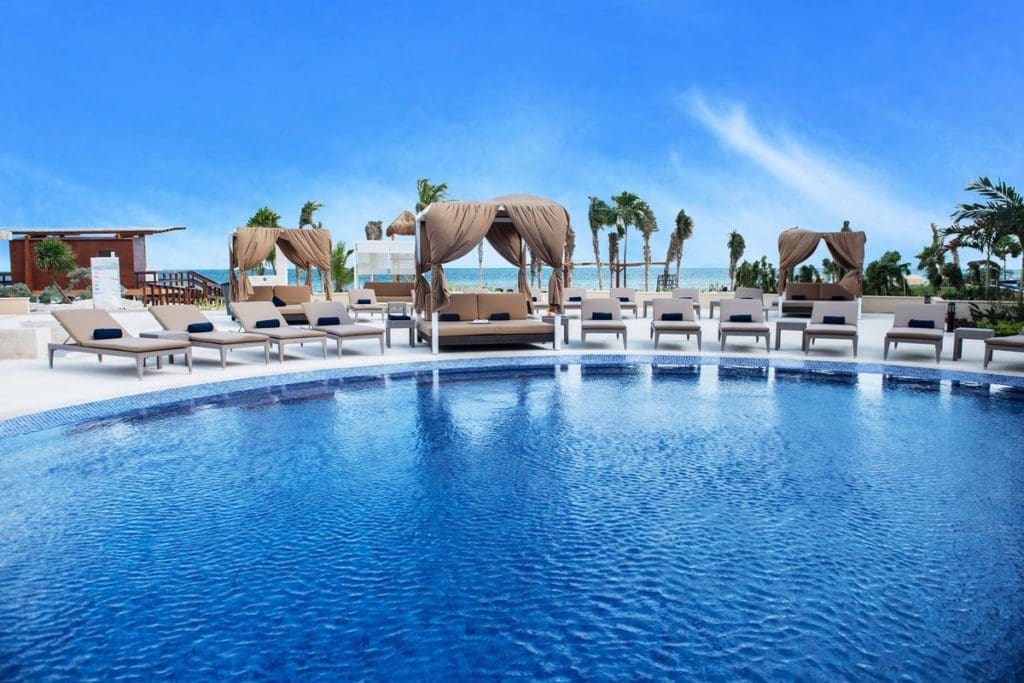 A large pool at Royalton Riviera Cancun, with cabanas and beach loungers flanking the pool and swaying palms in the distance.