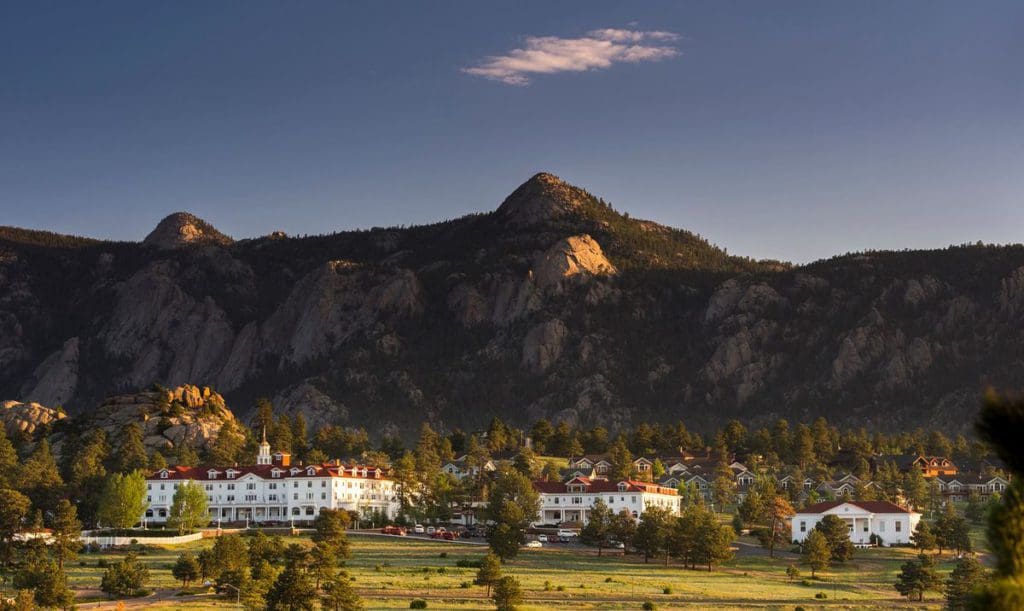 The Stanley Hotel standing proudly amongst the trees with mountains in the distance.