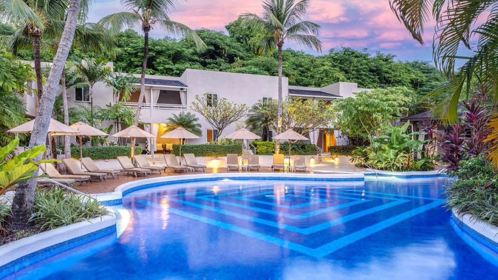 The pristine pool and pool deck at Waves Hotel and Spa by Elegant Hotels, with resort buildings behind it at sunset.