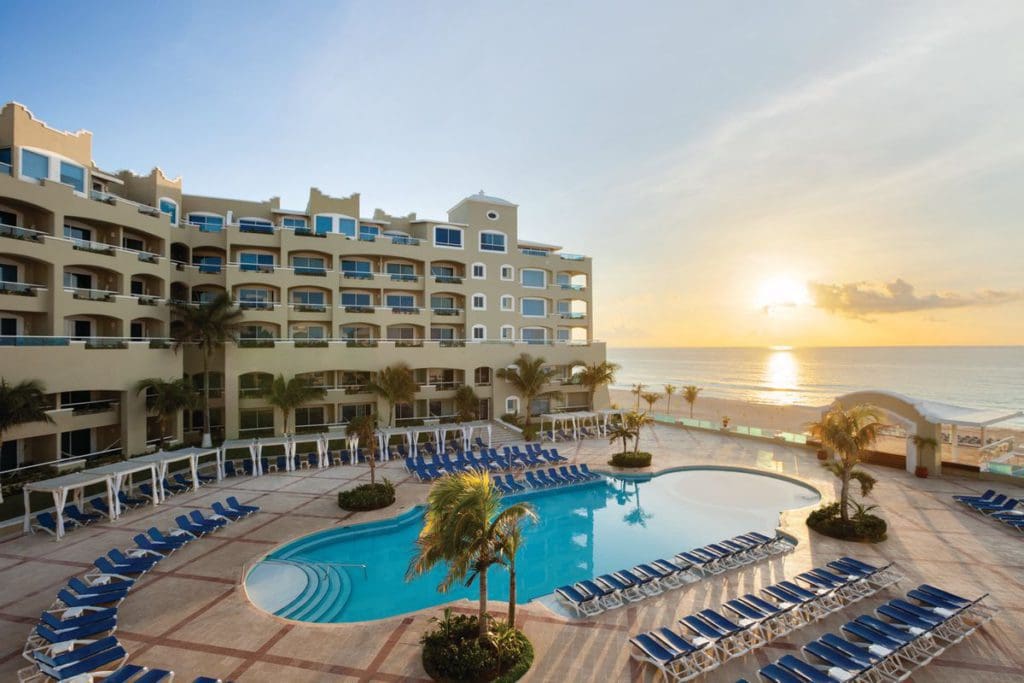 Wyndham Alltra Cancun resort building towering over the pool area and facing the ocean at sunset.