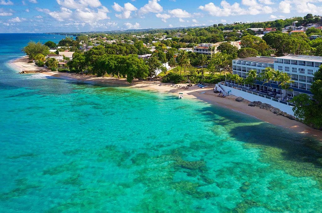 The turquoise ocean waters along the beach of the Waves Hotel and Spa by Elegant Hotels, with resort buildings in the distance.