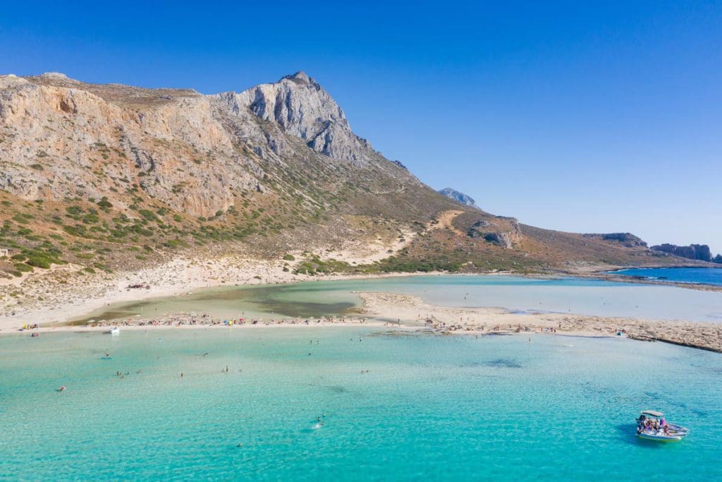 A boat hangs out in the waters off-shore from a stunning beach on Crete, one of the best Greek islands for families.