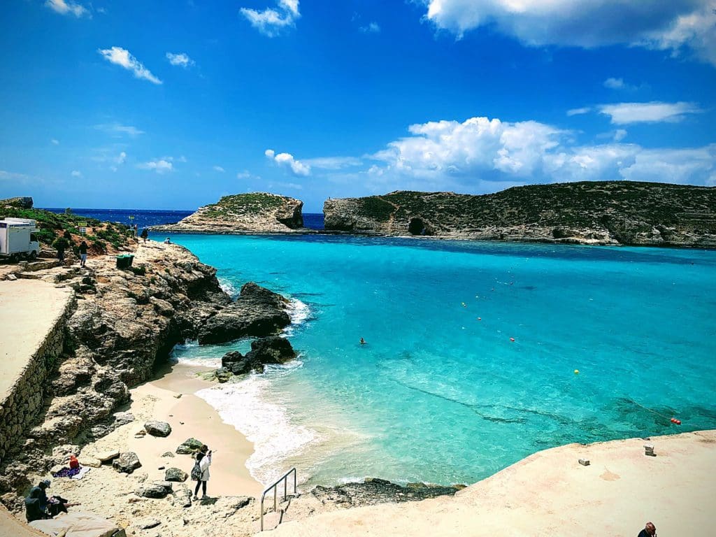 The Blue Lagoon in Malta, featuring a sandy shoreline, flanked by large rock formations and clear blue water.