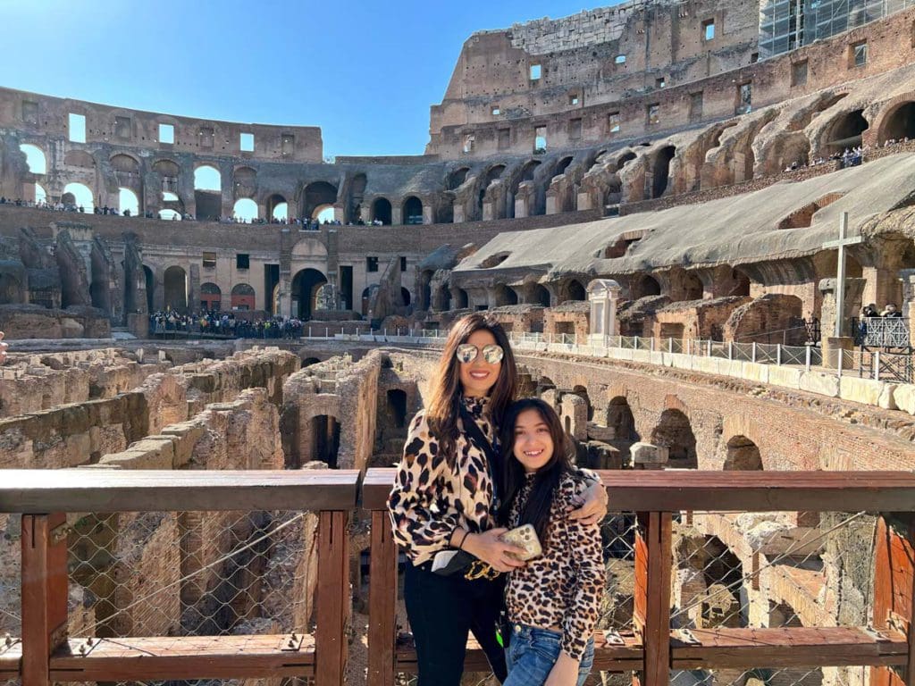 A mom and her daughter stand together inside the Colosseum, with a view of the underground corridors behind them.