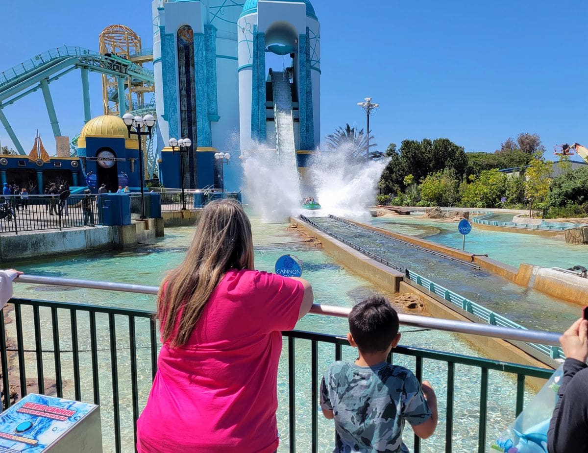 Two kids look over a fence at a water ride at SeaWorld San Diego.