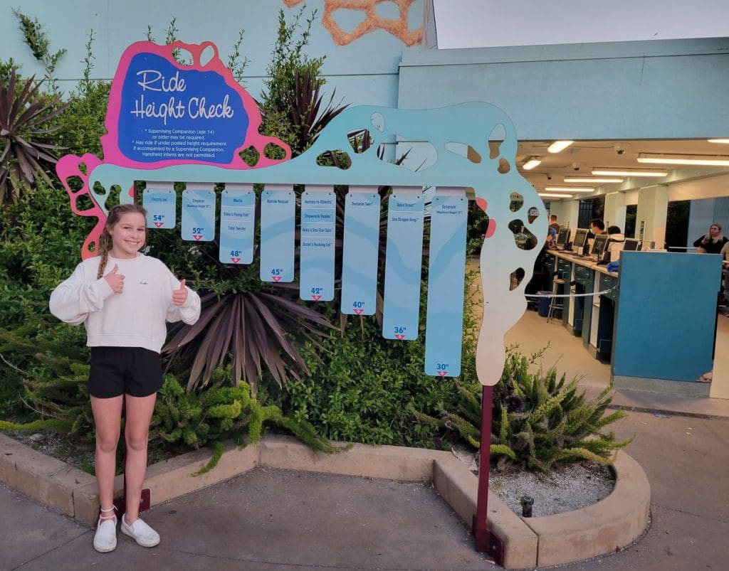 A teen girl stands in front of the board that measures ride height for eager kids at SeaWorld San Diego.