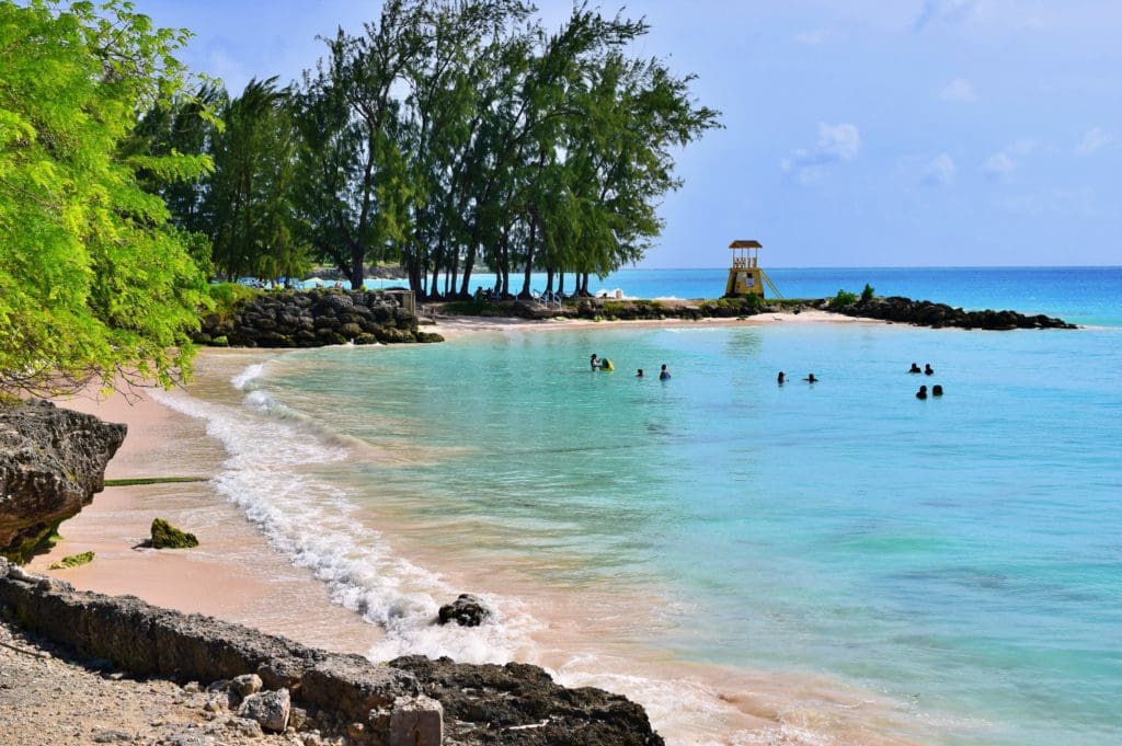 A stretch of beach in Barbados, with several people swimming off-shore.