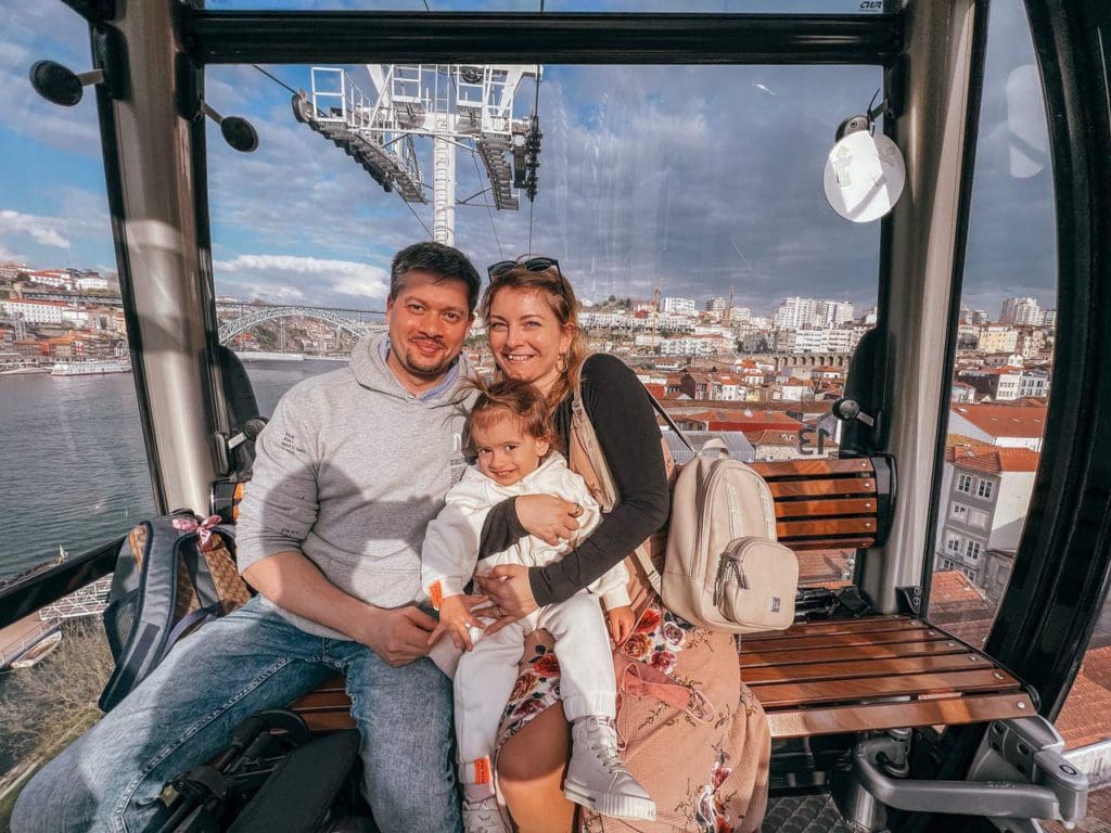 A family of three sits together and smiles in the Porto cable car, a must do on our 1-Week Porto itinerary with toddlers.
