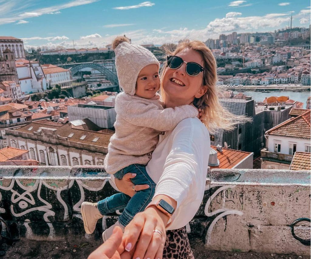 A mom holds her toddler, with a view of Porto in the distance. Porto is one of the best places to visit in Portugal with kids! 