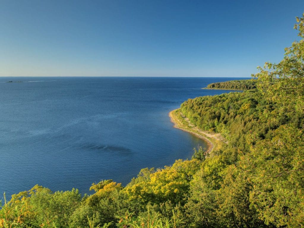 A scenic look over a shoreline of lush green trees along Lake Michigan in Peninsula State Park in Wisconsin.