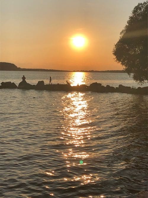 Three kids play follow the leader across large boulder in Sturgeon Bay at sunset.