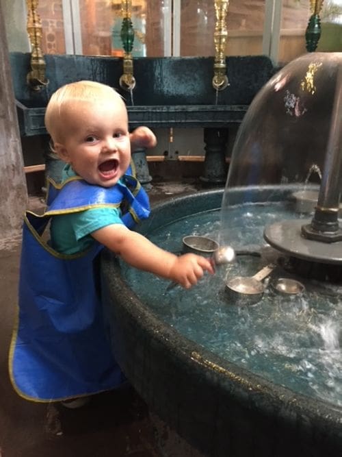 A toddler boy plays in the water at the Madison's Children's Museum in Madison, Wisconsin, one of the best affordable summer vacations in the United States with kids.