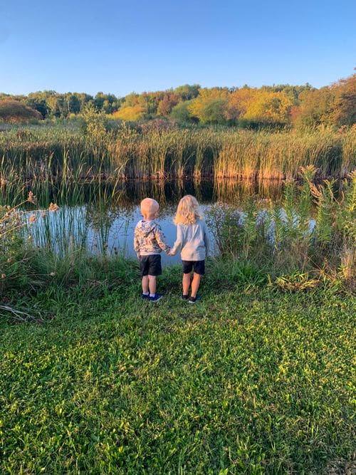 Two toddlers hold hands while looking at a small pond at Blue Vista Farm in Bayfield.