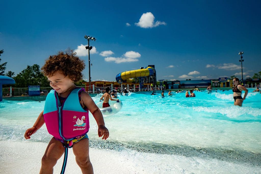 A young girl walks in front of the wave pool at Noah’s Ark Waterpark, with large water slides in the distance, one of the best places to visit in Wisconsin for families.