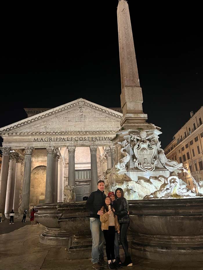 At night, two parents and their two kids stand outside of the Pantheon.