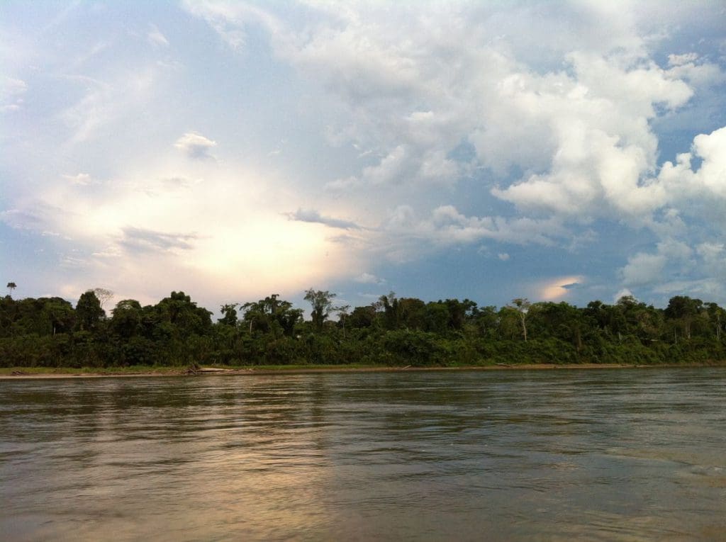 A scenic view of the river, and tree-lined shore within Manu National Park, a stunning stop on our Peru family vacation itinerary.