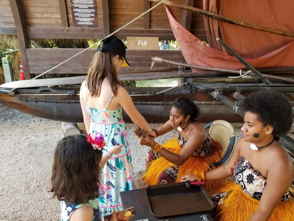 A young girl gets her arm painted during an interactive lesson at the Polynesian Culture Center, one of the best things to do in Oahu with kids.