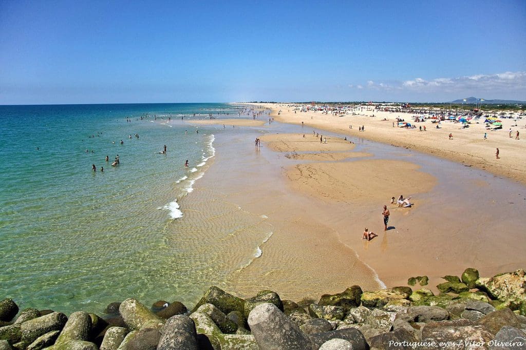 A long stretch of beach in Tavira, dotted with people on a sunny day, one of the best beach destinations in Europe for families.