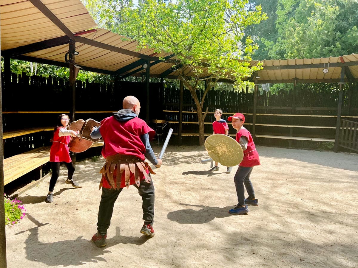 Two kids and two instructors practice gladiator fighting during a family-friendly class in Rome, Italy, one of the top places in travel in 2023 with kids.