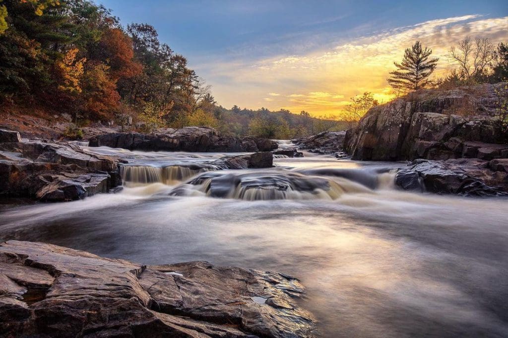 Big Falls flowing over rocks at Big Falls County Park, with fall foliage flanking both sides of the waterfall, in Eau Claire, one of the best places to visit in Wisconsin for families.