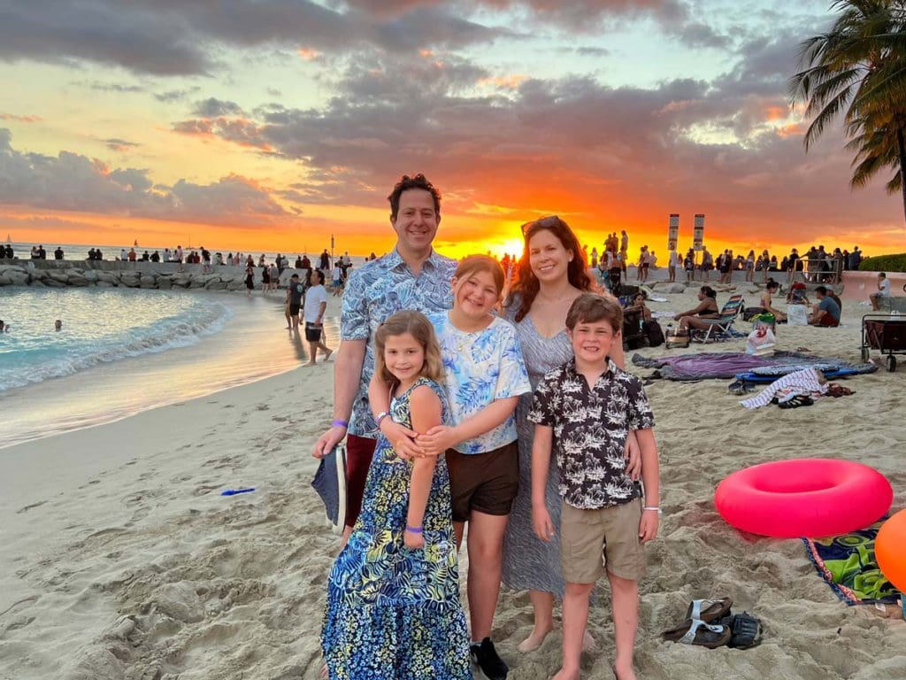 A family of four stands together on Waikiki Beach at sunset.